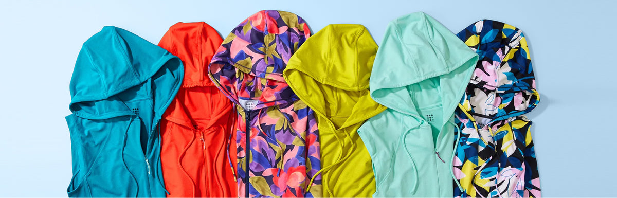 Five hooded jackets or windbreakers arranged side by side on a light blue background, shown in different colorways: teal, coral-red, multicolor floral, bright yellow, mint, and dark floral.