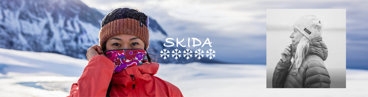A promotional banner for SKIDA winter wear, featuring a woman in a snowy mountain setting wearing a red jacket, a brown knit beanie, and a pink patterned face covering, alongside a black-and-white inset of another woman in winter clothing. The brand name 'SKIDA' is displayed in the center.