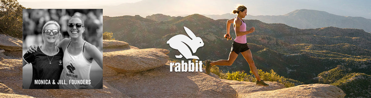 A wide outdoor scene shows a woman running on a rocky mountain trail with hills and trees in the background. A large white rabbit logo with the word 'rabbit' appears in the center, and a small inset photo on the left shows two women labeled 'MONICA & JILL, FOUNDER'.