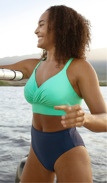 A woman outdoors by the water wearing a two-piece swimsuit with a mint green ruched bikini top and navy blue bikini bottoms.