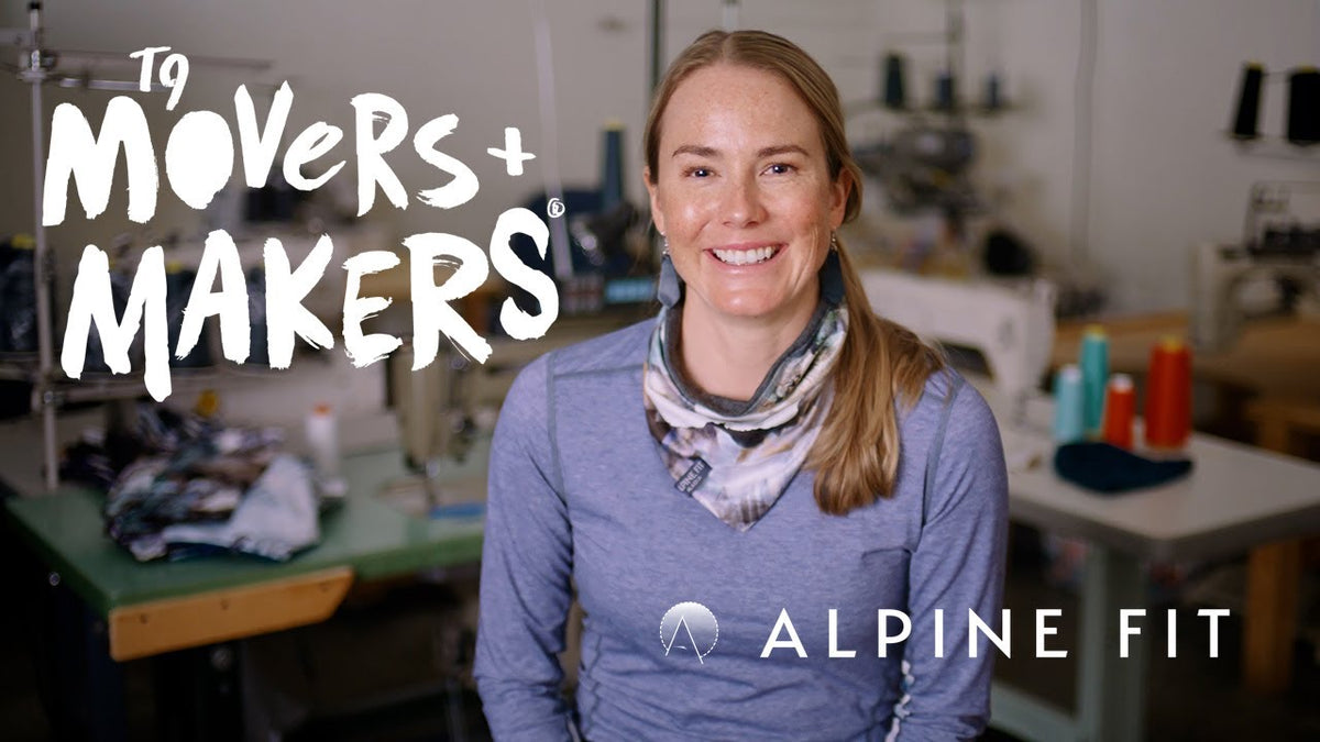 A smiling woman stands in a sewing workshop wearing a heathered blue long-sleeve top and a patterned scarf. Large text on the left reads 'To Movers + Makers' and text at the bottom reads 'Alpine Fit'.