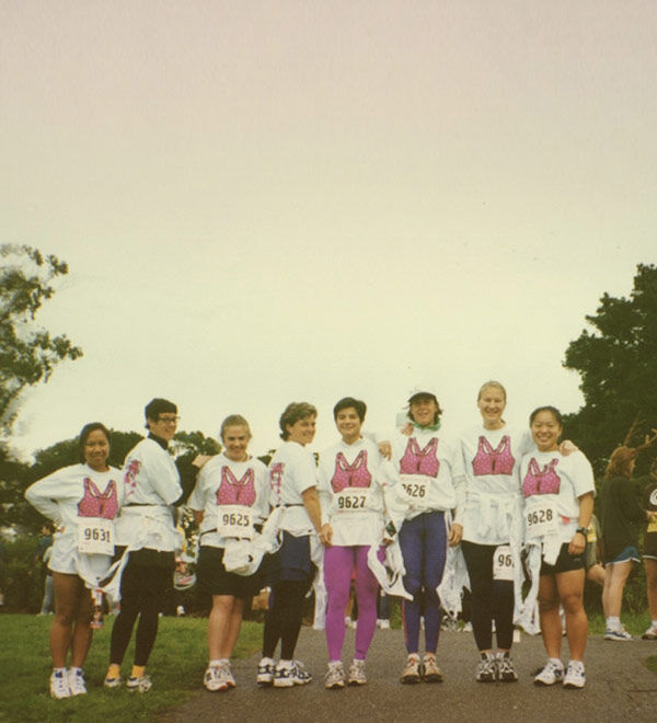 A group of eight women standing together outdoors, wearing matching white t-shirts with a pink bunny graphic and race bib numbers - title nine